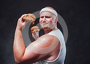 Funny fat men in the white bandage pulling a face with two hamburgers in his hands