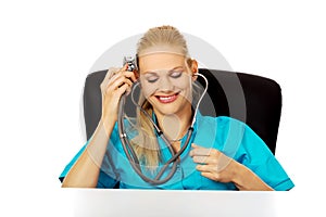 Funny female doctor or nurse sitting behind the desk with stethoscope