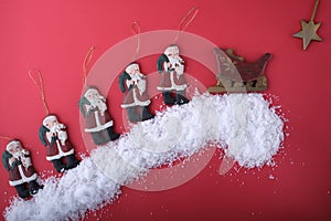 Funny figures of Santa Clauses go one after another up the snowy hill to the sleigh with gifts.