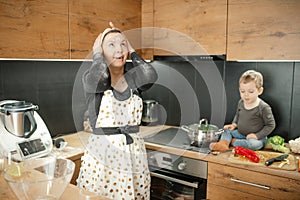 Funny floury shocked woman in handkerchief look up, holding head near little boy in flour because of mess in the kitchen