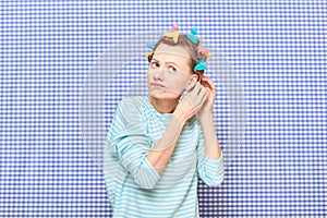 Funny focused young woman is putting her hair into colorful curlers