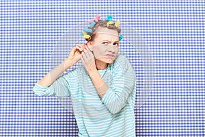 Funny focused young woman is putting her hair into colorful curlers