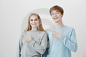 Funny friendly siblings showing direction to moms guest. Attractive brother and sister with fair hair, pointing left