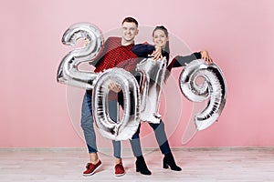 Funny friends girl and guy dressed in stylish clothes are holding balloons in the shape of numbers 2019 on a pink