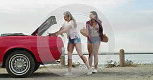 Funny friends open boot with skateboard at beach, smile and walking outdoor. Happy women on car trunk for skating