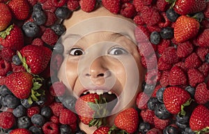Funny fruits. Strawberry, blueberry, raspberry, blackberry background on child face. Healthy kids eating. The kids face