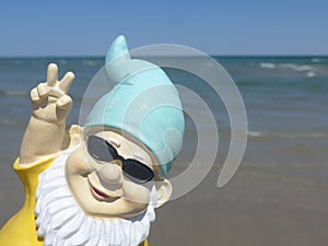Funny garden gnome with sunglasses seaside makes peace sign