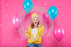 Funny girl in birthday hat, balloons and flying confetti on pastel pink background. Attractive teenager celebrating birthday.