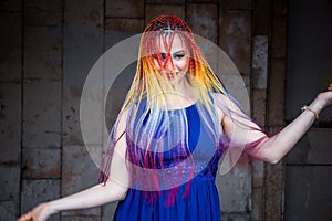 A funny girl with bright makeup and colored braids in a light blue dress is spinning and laughing cheerfully on the