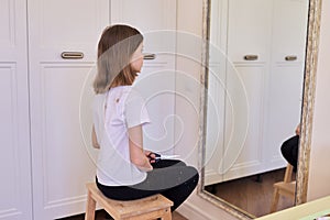 Funny girl child cutting her hair with scissors sitting at home in front of mirror