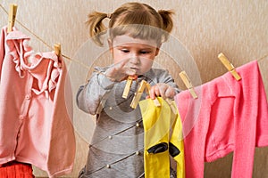 Funny girl with clothespin and the clothesline. Baby pink clothes dry on a rope. baby hangs yellow socks and a pink sweater.