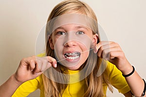 Funny girl with dental braces flossing her teeth. Close-up portrait of pre teen girl with dental floss isolated.