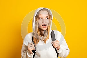 Funny girl dressed white hoodie on yellow  background with backpack. Portrait of cool schoolgirl with backpack