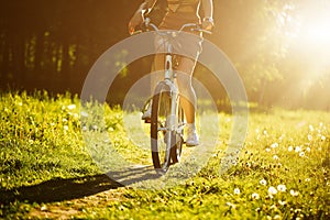 Funny girl driving bicycle outdoor. Sunny summer lifestyle concept. Woman in dress and hat in Field with dandelions