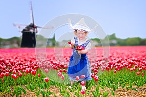 Funny girl in Dutch costume in tulips field with windmill