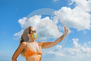 Funny girl in face mask taking selfie photo on beach