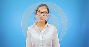 Funny girl in glasses jumps into the frame, greets, waves her hand and disappears. Blue background, student, comical.