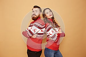 Funny girl and a guy dressed in red and white sweaters with deer stand back to back on a beige background in the studio