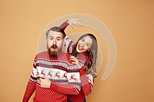 Funny girl and a guy dressed in red and white sweaters with deer stand together on a beige background in the studio
