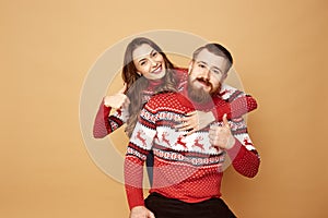 Funny girl and a guy dressed in red and white sweaters with deer stand together on a beige background in the studio