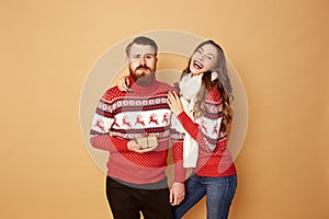 Funny girl and a guy dressed in red and white sweaters with deer stand together on a beige background in the studio