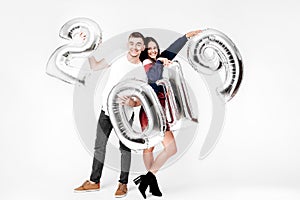 Funny girl and guy dressed in a stylish smart clothes are holding balloons in the shape of numbers 2019 on a white