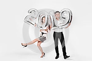 Funny girl and guy dressed in a stylish smart clothes are holding balloons in the shape of numbers 2019 on a white