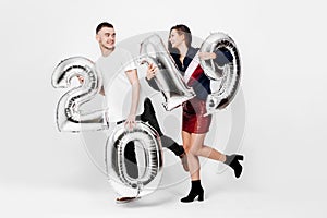 Funny girl and guy dressed in a stylish smart clothes are holding balloons in the shape of numbers 2019 on a white