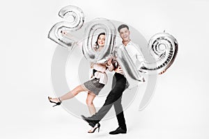 Funny girl and guy dressed in a stylish smart clothes are holding balloons in the shape of numbers 2019 on a white