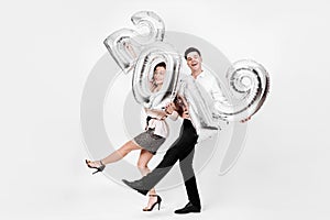 Funny girl and guy dressed in a stylish smart clothes are holding balloons in the shape of numbers 2019 on a white