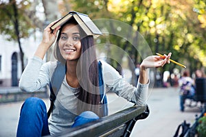 Funny girl holding book on head outdoors