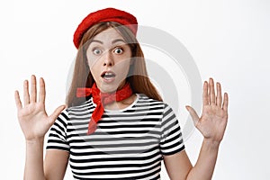 Funny girl mime look surprised as raising hands, leaning on invisible wall during pantomime performace, wearing red