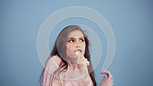 Funny girl in pink sweater having fun, dancing, jumping and singing to yellow lollipop. Portrait of a pretty young girl