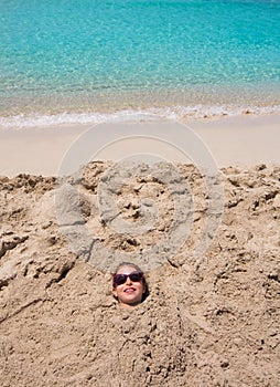 Funny girl playing buried in beach sand smiling sunglasses