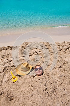 Funny girl playing buried in beach sand smiling sunglasses