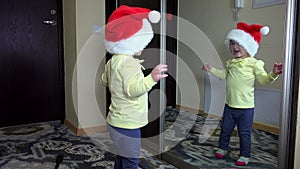 Funny girl put santa hat on head and jump in front of mirror. Careless childhood