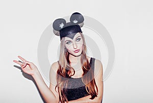 Funny girl show peace sigh represents a small cat or mouse. Woman with a bright makeup hairstyle and night dress mouse ears having
