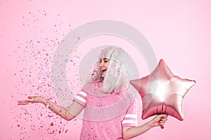 Funny Girl with silver hair gives a smile and emotion on pink background. Young woman or teen girl with balloons and confetti