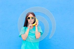 Funny Girl with Sunglasses and Banana Phone on Blue Background