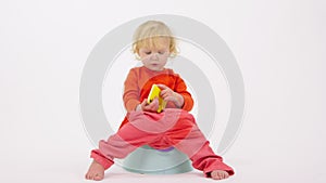 Funny girl toddler sits on child's potty explore smartphone on white background