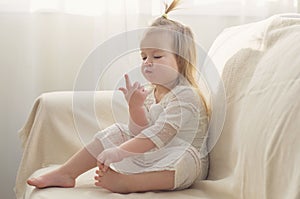 Funny girl toddler in white dress with a tail sitting on the sofa at home