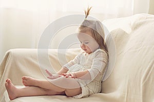 Funny girl toddler in white dress with a tail sitting on the sofa at home