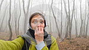Funny girl traveler while walking through a dangerous foggy forest. Crooked trunks of bare trees in a thick fog. The woman`s hair