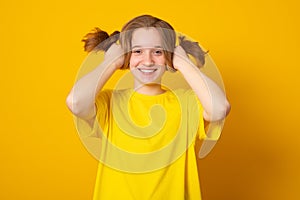 Funny girl with a two-ponytail hairstyle smiles grimaces and laughs on a yellow background