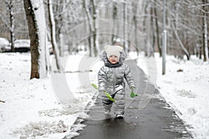 A funny girl in a warm silver jumpsuit runs along the path in winter