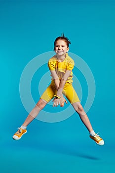 Funny girl wears yellow sportswear jumping on a colored blue background