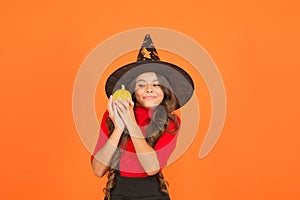 Funny girl in witch costume hat for Halloween with pumpkin or squash on orange background, halloween food