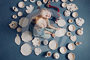 Funny girls with closed eyes sitting on the floor with many clay products.