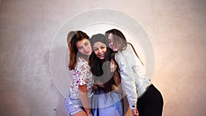 Funny girls pose in camera with smiles on their faces and stand against background of light wall in room.