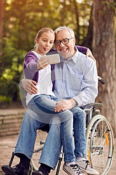 Funny granddaughter using phone for selfie with her disabled fat